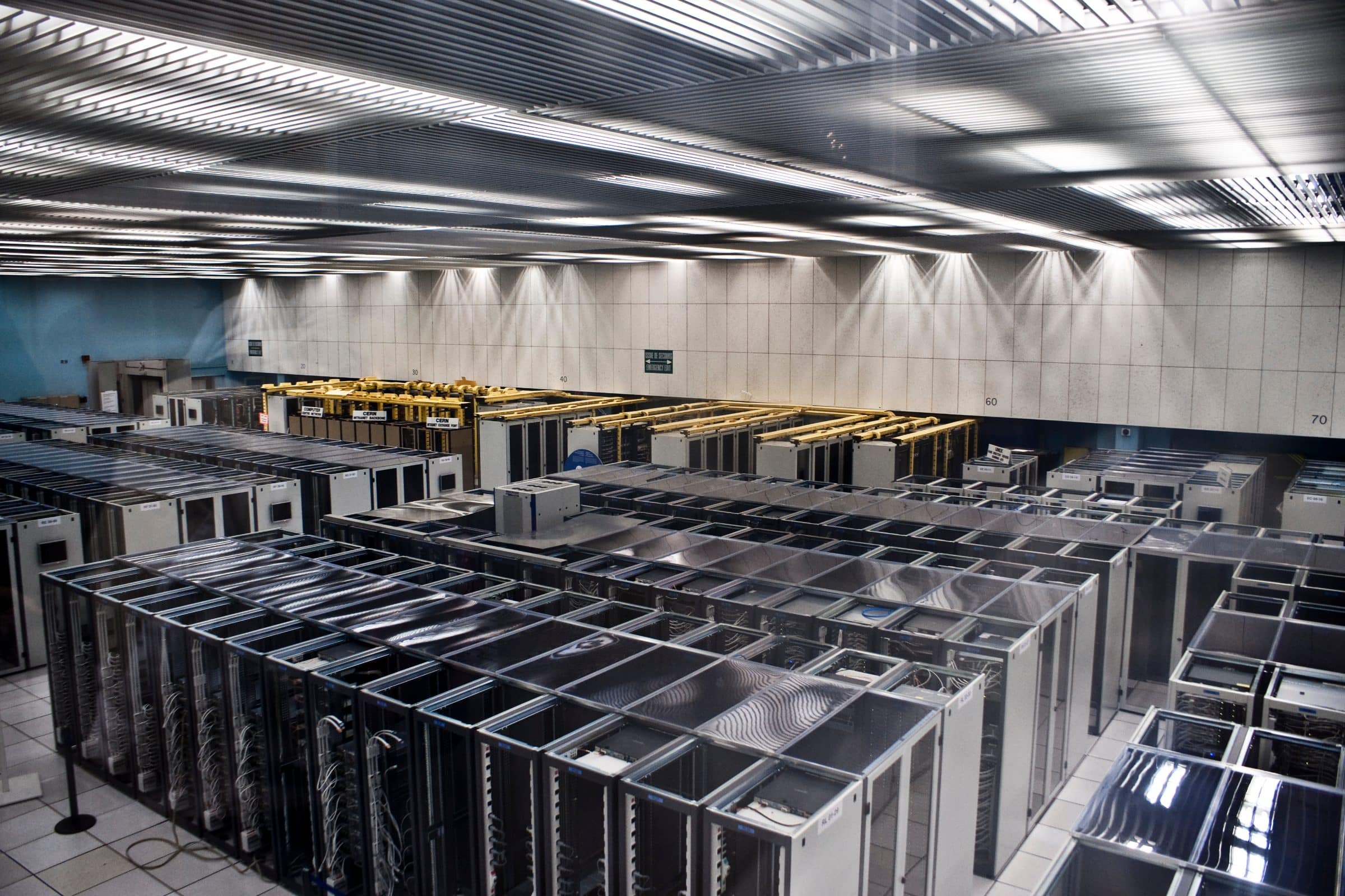 Rows of server racks receding down a data-centre aisle under bright ceiling lights.