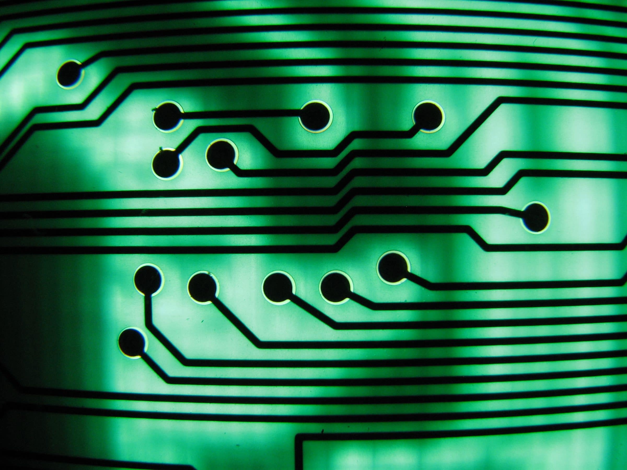 A close view of a green circuit board, its copper tracks running in straight lines and right angles between round solder pads.