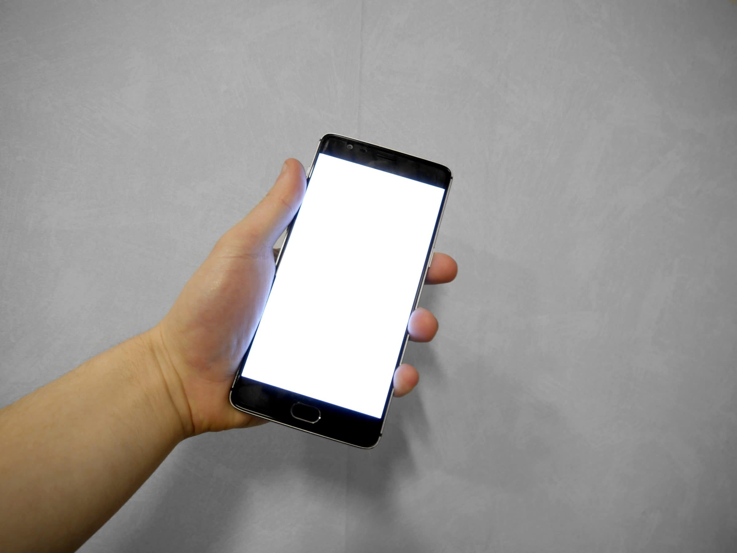 A hand holding a smartphone with a blank white screen.