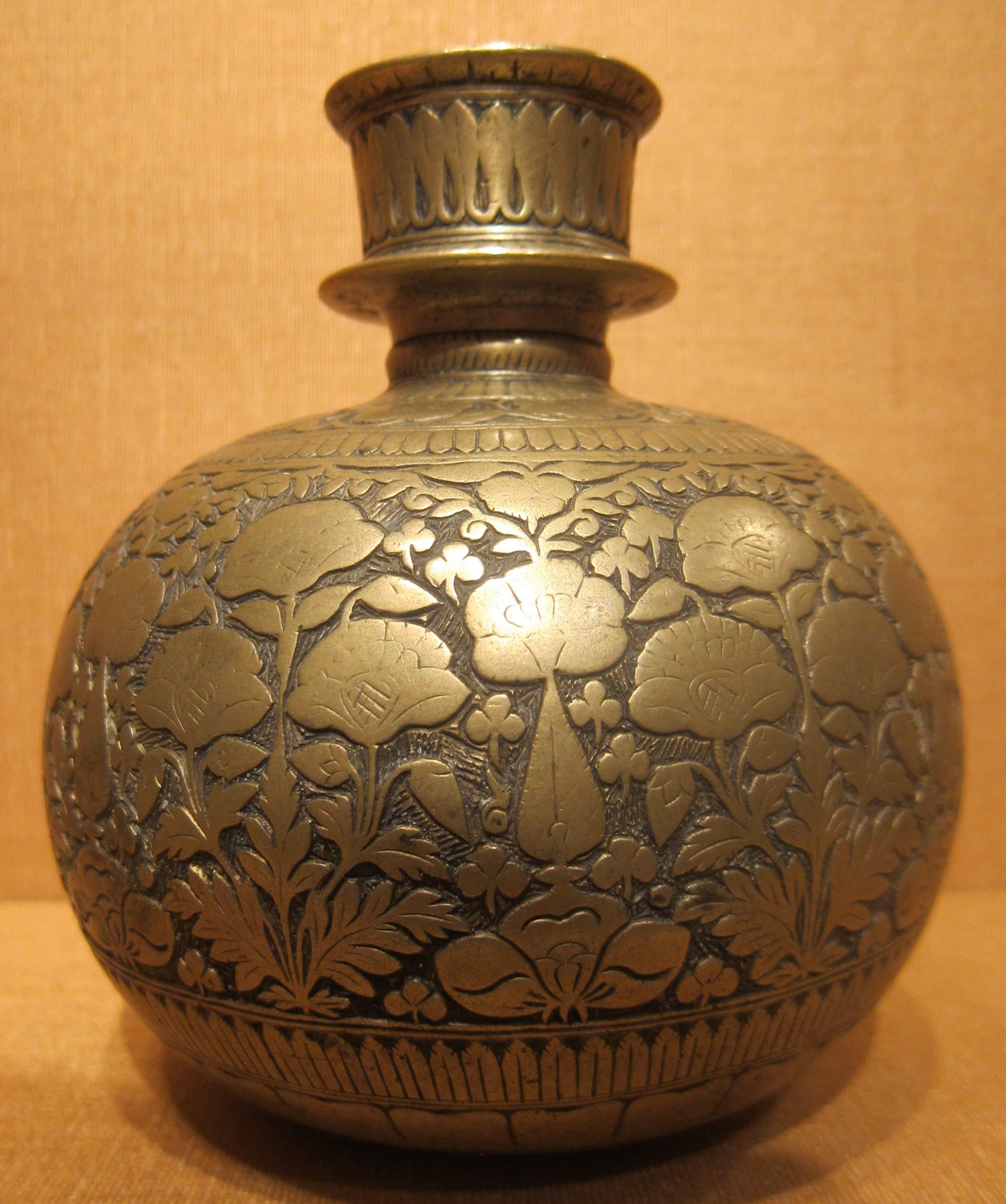 An engraved brass vessel with a rounded body and a flared neck, photographed against a plain ground.